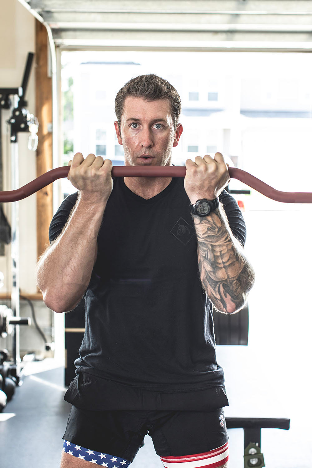 The Edge Bar is a mix between a shortened cambered bar and an EZ Bar. Perfect for enhanced bicep workouts, chest workouts, and more. This image presents the Edge Rackable Cambered Bar being used by a man for a bicep workout.