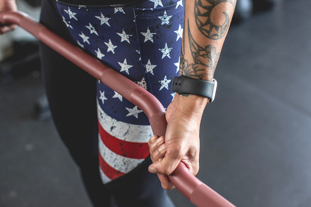 The Edge Bar is a mix between a shortened cambered bar and an EZ Bar. Perfect for enhanced bicep workouts, chest workouts, and more. This image presents a close-up shot of the Edge Rackable Cambered Bar being used for a workout.