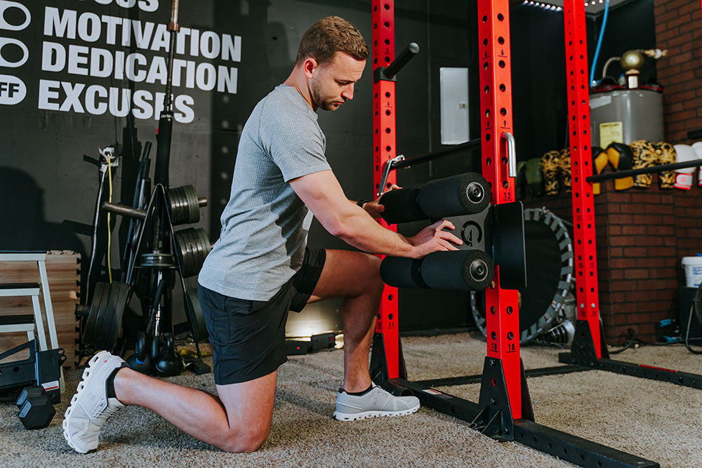 This Rack Mounted Glute Ham Developer is less bulky and lower priced than conventional GHDs. Perfect for glute workouts, ab workouts, and hamstring workouts. This image presents the Rack Mounted Glute Ham Developer being attached to a red power rack in a home gym.
