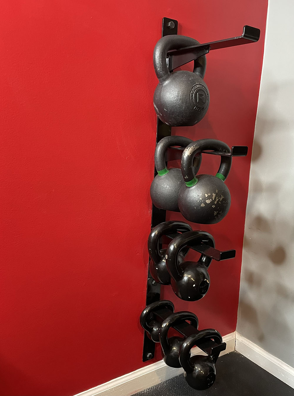 The Wall Mounted Kettlebell Storage Rack was created to provide storage solutions for your kettlebells and get your weights off the ground. This image presents the Wall Mounted Kettlebell Storage Rack in use with several kettlebells hanging from the rack.